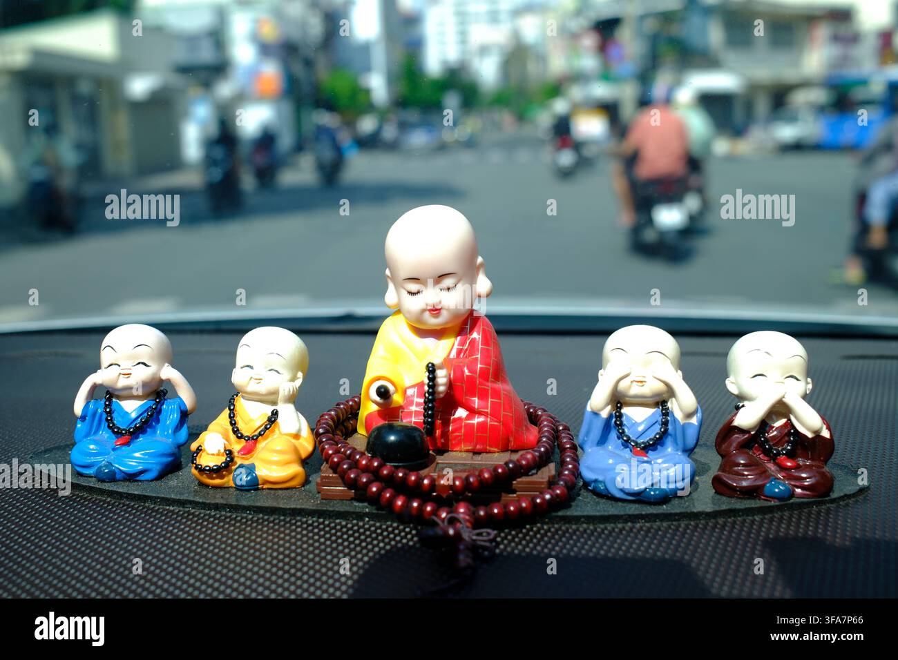 Lächelnde Miniatur-Mönchstatuetten in Gewändern, die als Glücksbringer auf einem vietnamesischen Auto-Armaturenbrett platziert werden. Ho-Chi-Minh-Stadt. Vietnam. Stockfoto
