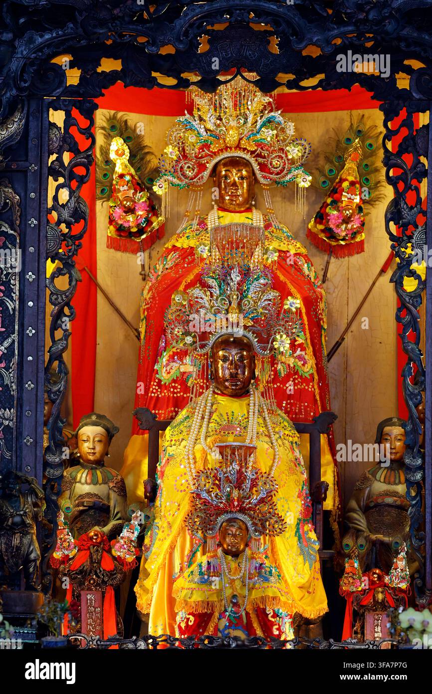 Ba Thien Hau Tempel. Kunstvoller Holzschrein mit lackierten Schnitzereien umrahmt drei goldene taoistische Gottheiten-Statuen. Ho-Chi-Minh-Stadt. Vietnam. Stockfoto