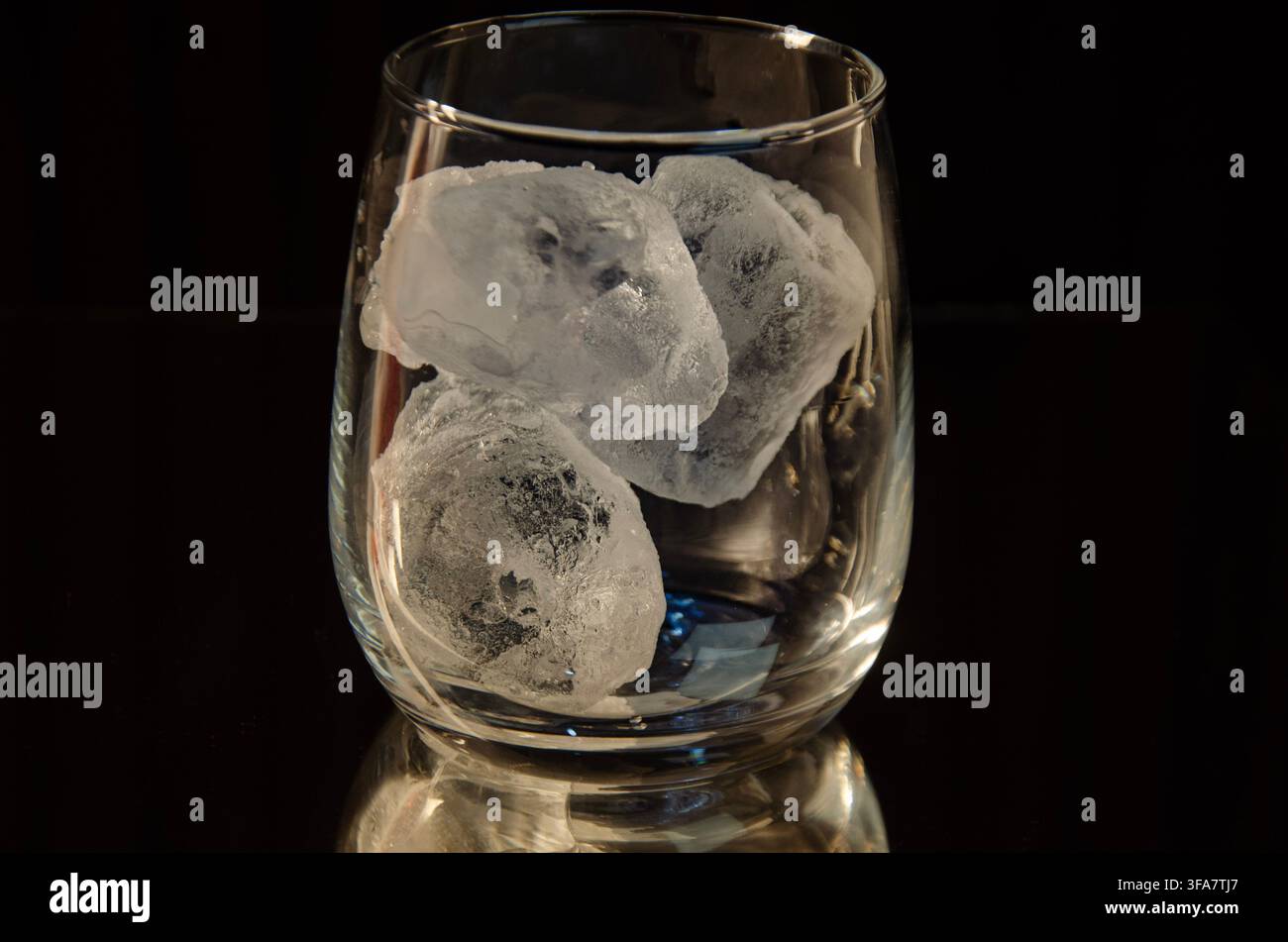 Klares Glas mit Eiswürfeln vor dunklem Hintergrund Stockfoto