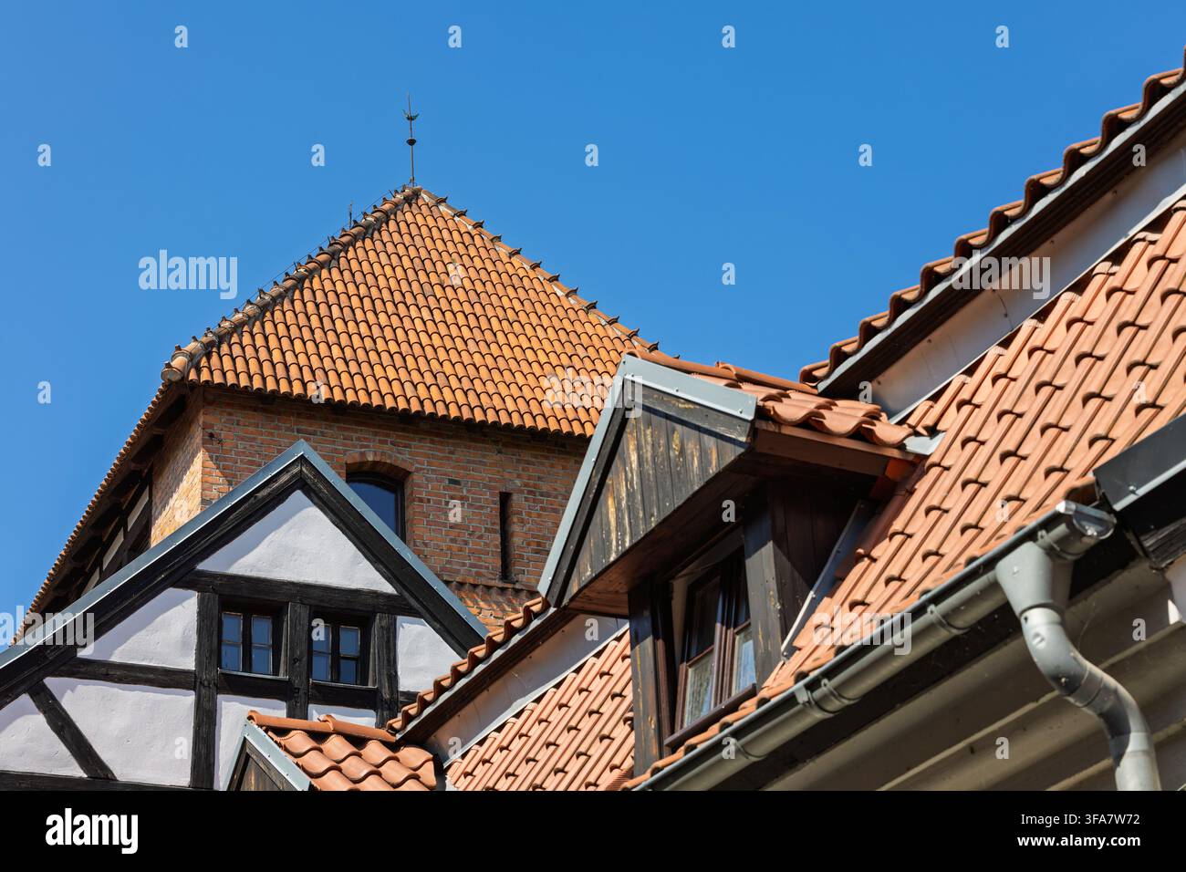 Ein historisches Gebäude in der Altstadt von Torun verfügt über steile Ziegeldächer, holzgerahmte Abschnitte und einen Backsteinturm mit einem spitzen Dach. Stockfoto