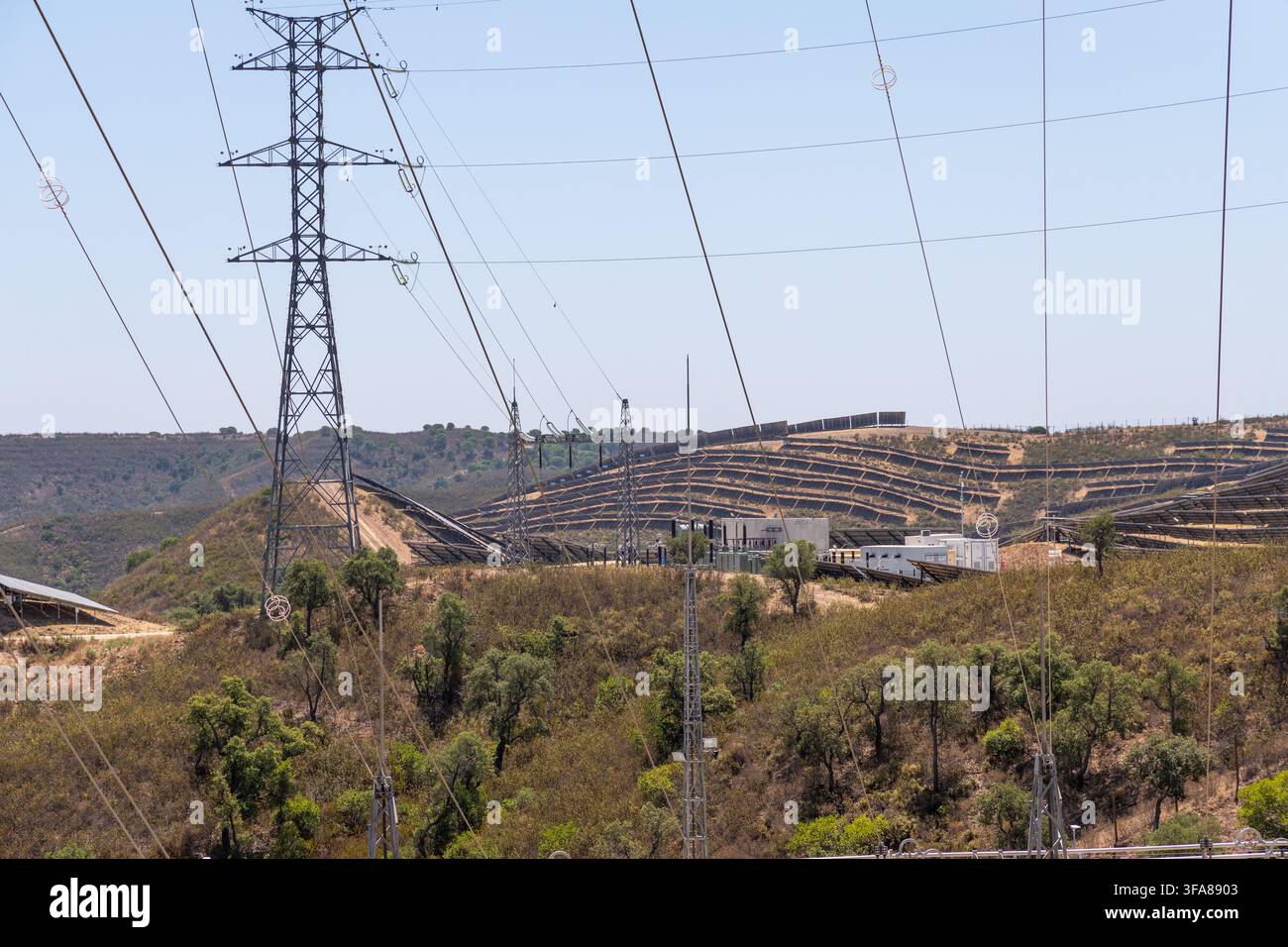 Reihen von Solarpanelen sind auf einem Hügel mit Stromübertragungsmasten und Leitungen im Vordergrund installiert Stockfoto