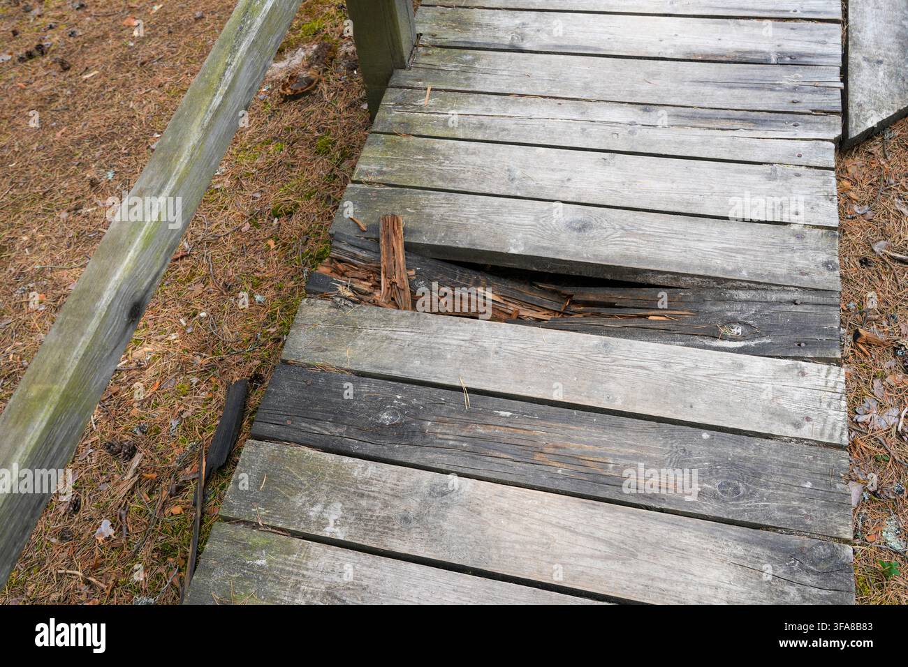 Nahaufnahme einer verwitterten hölzernen Wald-Fußgängerbrücke mit gebrochenen und verrotteten Planken, die Verfall, schlechte Instandhaltung und Gehweg-Sicherheitsrisiko zeigt Stockfoto