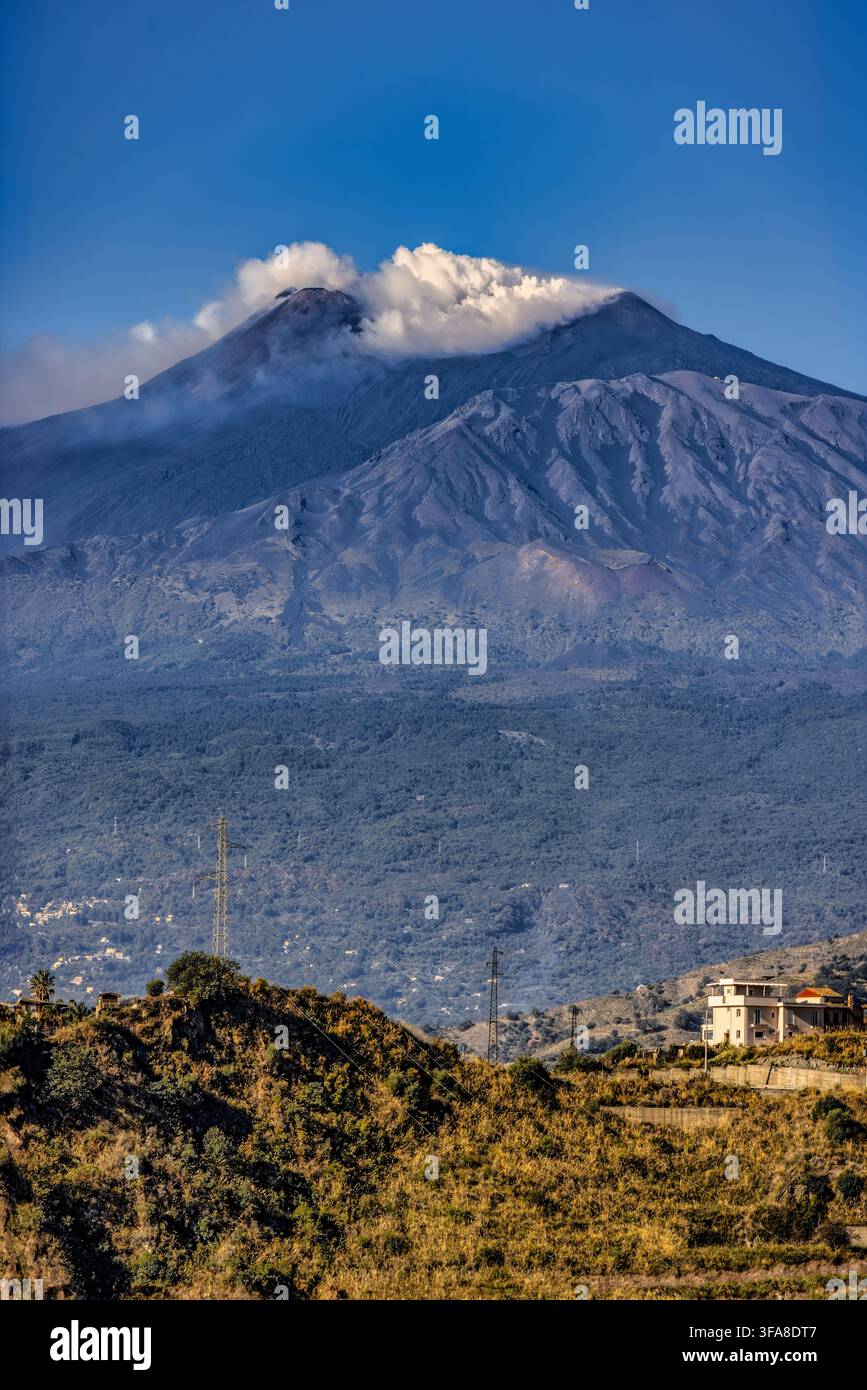 Der Ätna erhebt sich über die sizilianische Landschaft. Der massive Vulkankonus dominiert den Horizont unter einer weißen Wolkendecke. Stockfoto