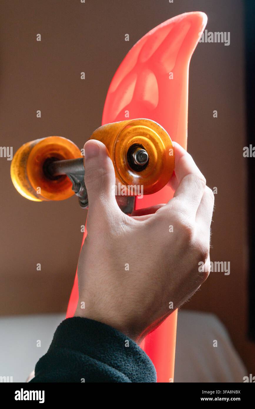 Hand, die das Rad und den Truck eines leuchtend orangefarbenen Skateboards einstellt Stockfoto