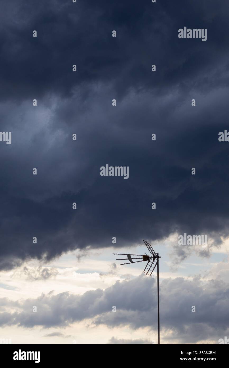 Eine Fernsehantenne als Silhouette vor massiven dunklen Sturmwolken und einer hellen Öffnung im Himmel. Die dramatische Wolkenformation schafft eine kraftvolle Sz Stockfoto