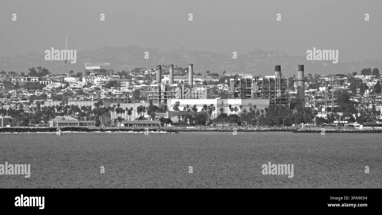 Schwarz-Weiß-Ansicht einer industriellen Uferzone. Stadtsilhouette mit Fabriken und Schornsteinen über das Wasser verteilt. Urbane Landschaft unter einem dunstigen Himmel. Geeignet für Stockfoto