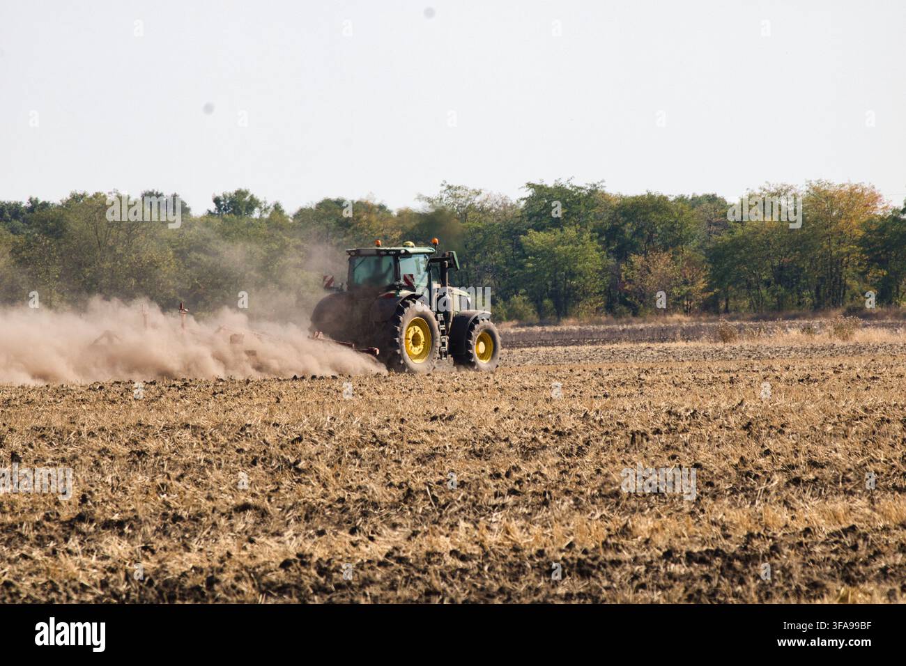Nahaufnahme Rückansicht eines modernen grünen Traktors, der trockenen Ackerboden bearbeitet und eine große Staubwolke aufwirbelt. Stockfoto