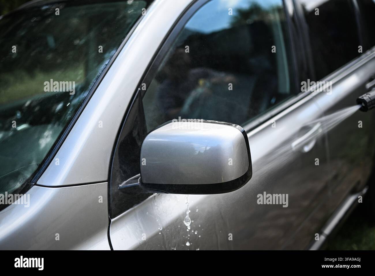 Hochdruck-Wasserstrahl spült Seitenspiegel und Tür eines grauen Autos im Freien, Fahrzeugreinigung, Autodetailierung, Wartung und Hochdruckreinigungskonzept. Stockfoto