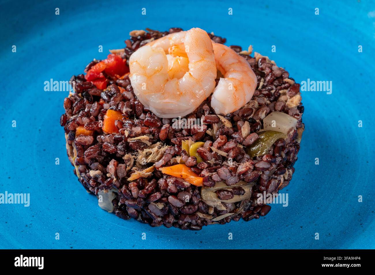 Schwarzer Venere-Reis mit Garnelen, Fisch und gemischtem Gemüse, darunter Karotten, Zucchini, Zwiebel und Paprika, serviert als Gourmet-Meeresfrüchteschüssel Stockfoto
