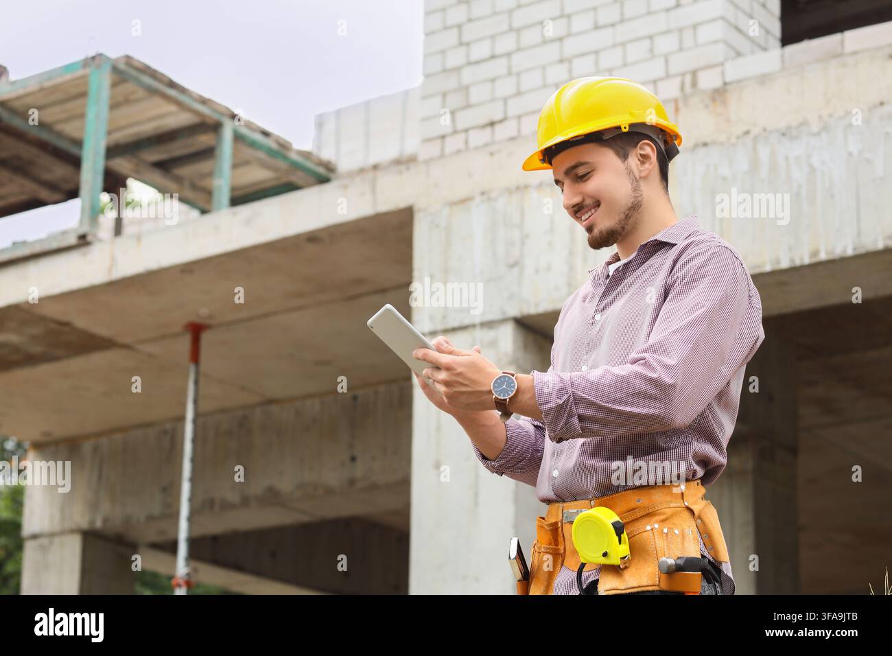 Bautechnologie und digitales Projektmanagement, lächelnder Ingenieur verwendet ein Tablet auf einer Baustelle Stockfoto