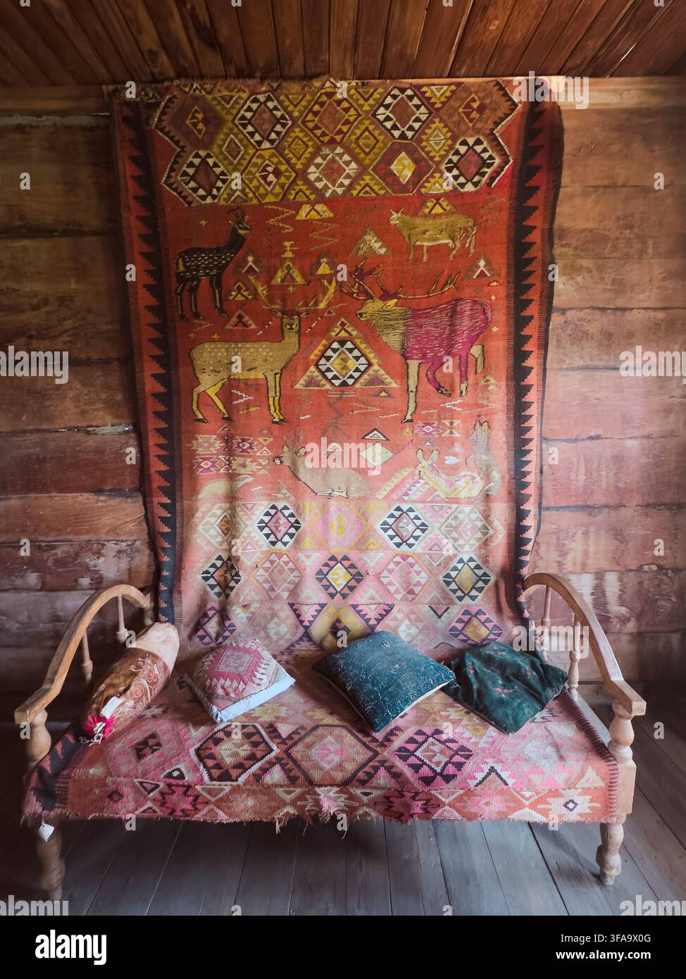 Innenansicht einer rustikalen Holzhütte mit einer traditionellen Holzbank, die mit farbenfrohen Kissen und einem ethnischen Teppich geschmückt ist. - Smartphone-aufgenommenes Stockfoto