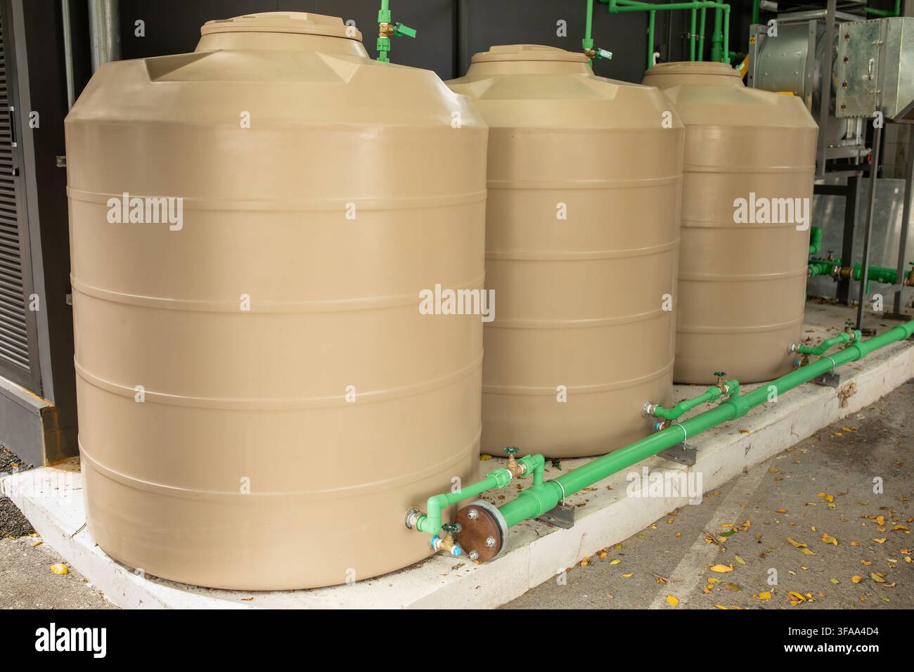 Drei große beige Kunststoff-Wasserspeichertanks, die durch Rohre an einer Außenanlage verbunden sind, Industrie-Wasserversorgungskonzept Stockfoto
