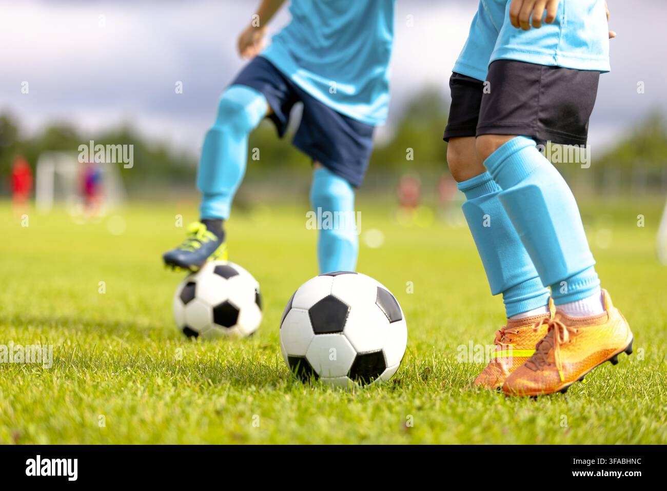 Nahaufnahme von Junior-Fußballern in blauen Trikots, die Ballkontrolle und Dribbling-Übungen auf einem grünen Rasenplatz üben Stockfoto