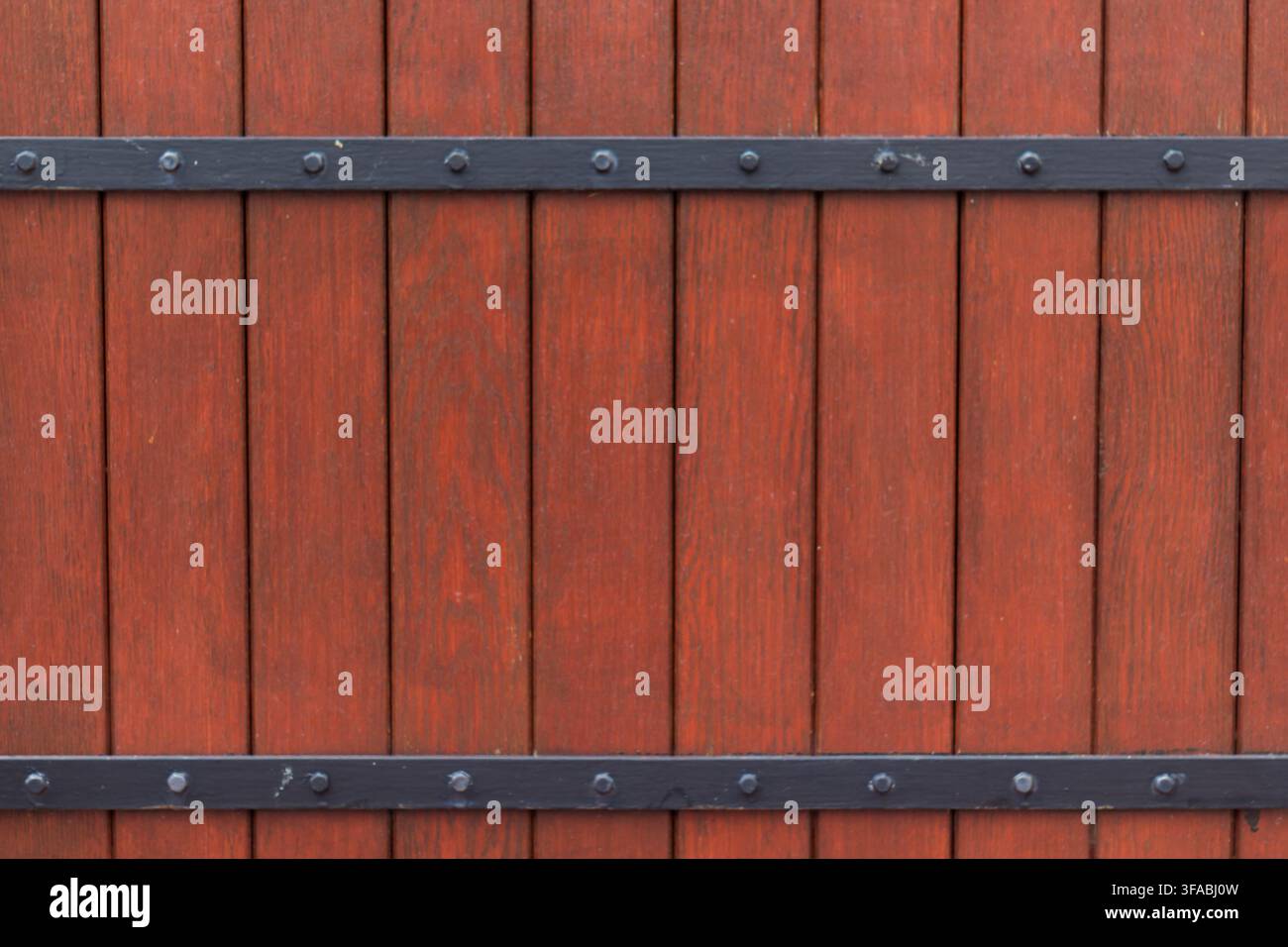 Rotes Holztor mit schwarzen Metallscharnieren und dekorativen Beschlägen. Stockfoto