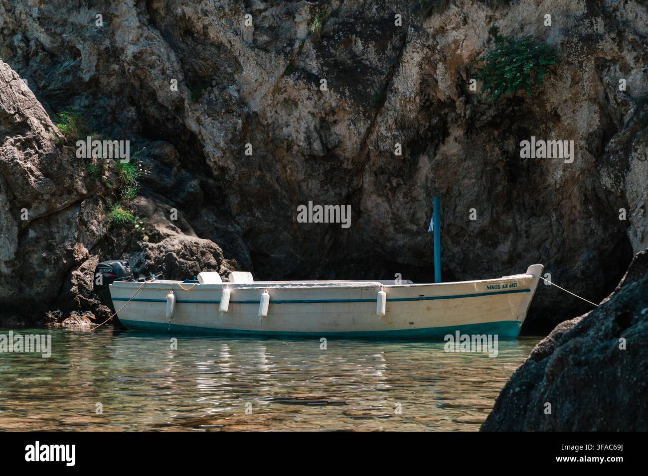Ein traditionelles Holzfischboot mit einem blaugrünem Rumpf ruht im klaren Wasser neben den schroffen Felsen einer mediterranen Küstenbucht Stockfoto