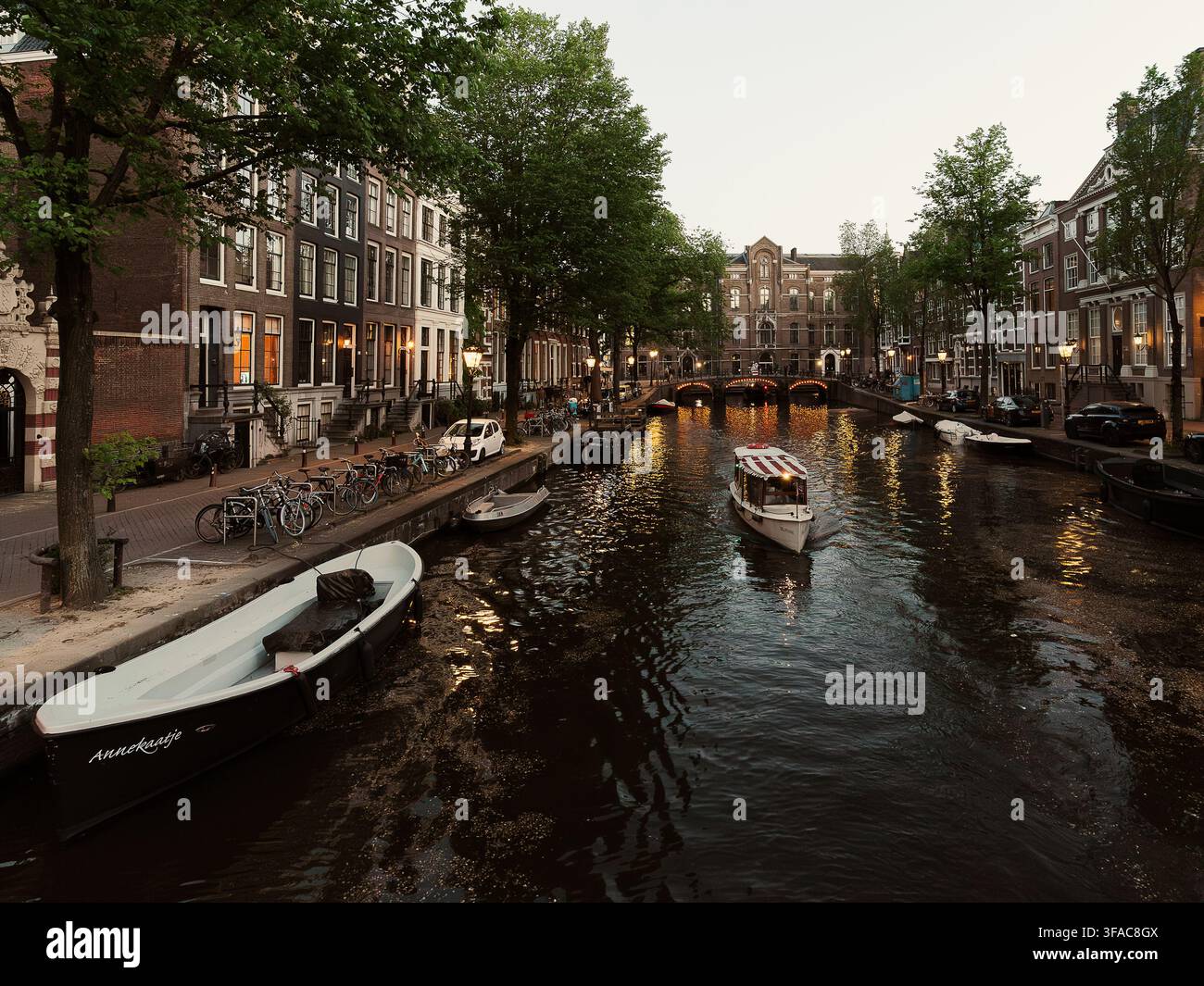 Atmosphärischer Kanalblick mit Booten und beleuchteten Brücken in der Dämmerung in Amsterdam Stockfoto