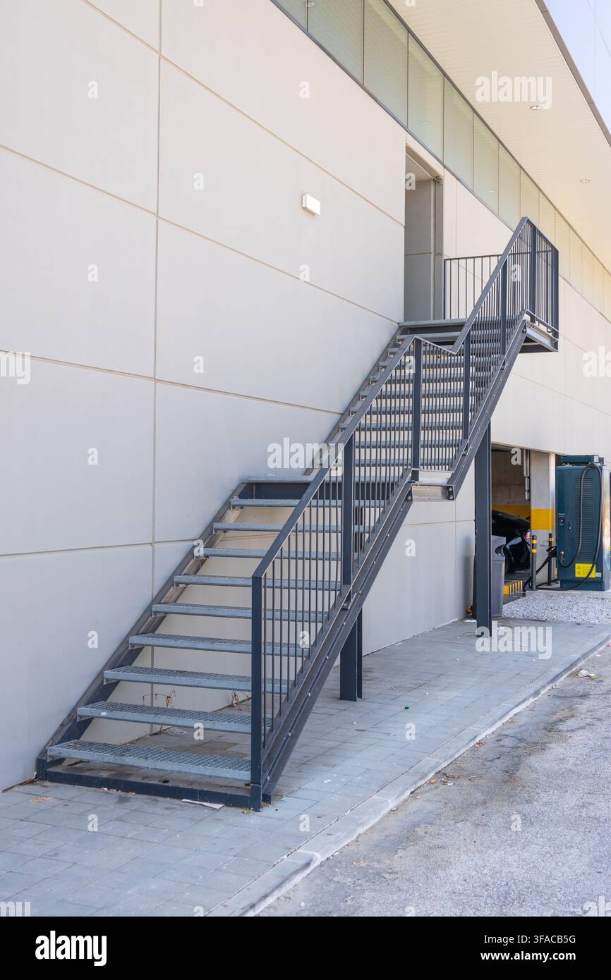 Eine zweckmäßige Metalltreppe mit Sicherheitsgeländern steigt zu einer Tür an der Außenseite einer modernen Gebäudestruktur hinauf Stockfoto