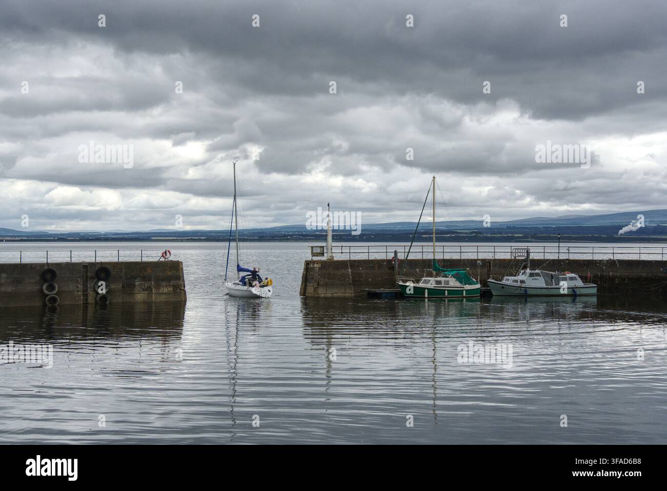 Scenische Aussicht, eingerahmt von den Steinmauern des Piers an der Mündung des Avoch Harbour, zeigt eine Segeljacht, die hinaus auf die offene See des Moray Firth in Schottland fährt. Stockfoto