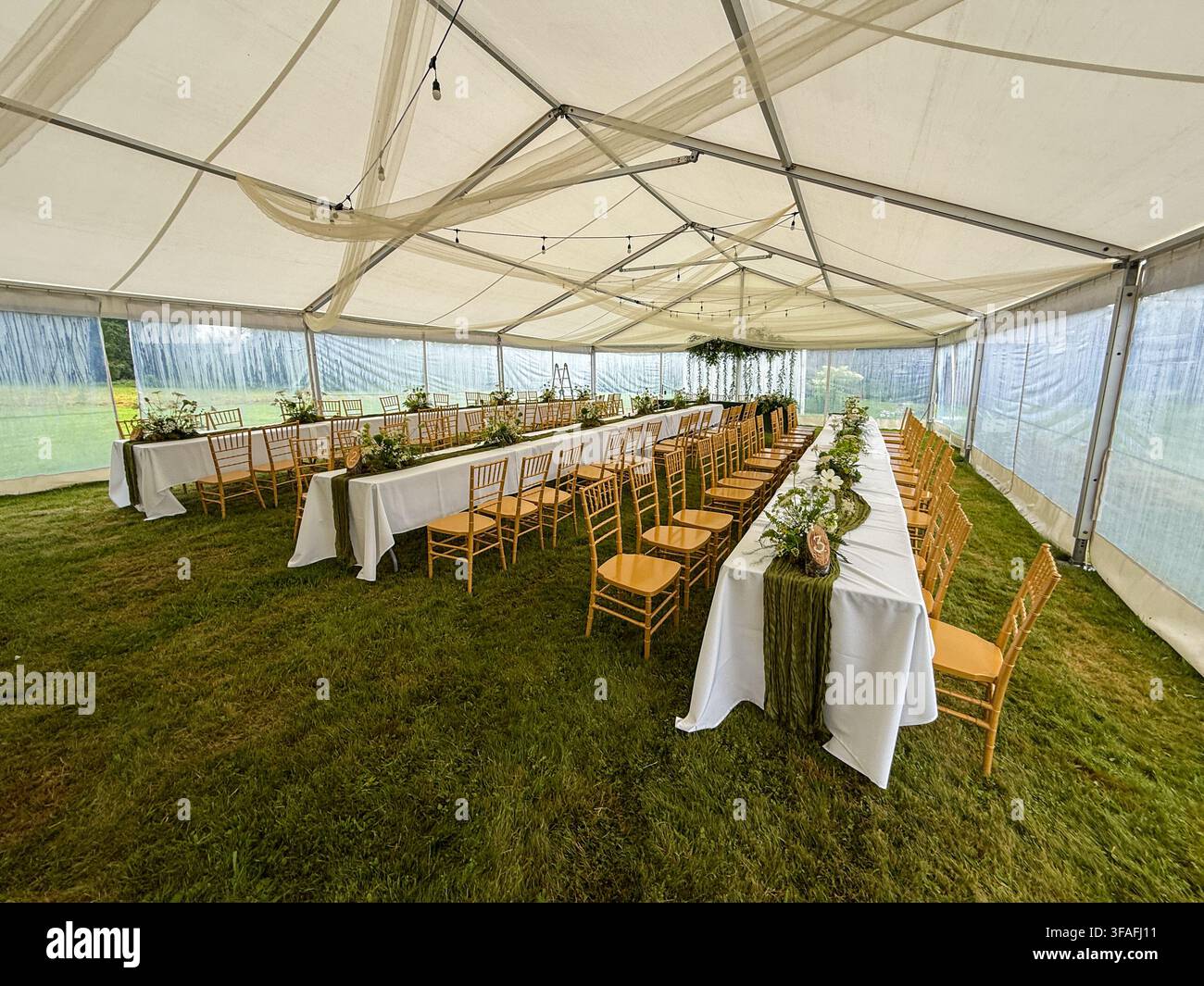Riga, Lettland - 1. August 2026: Elegante Hochzeitsempfang im Freien in einem geräumigen Festzelt mit langen Banketttischen, Holzstühlen, Flor Stockfoto