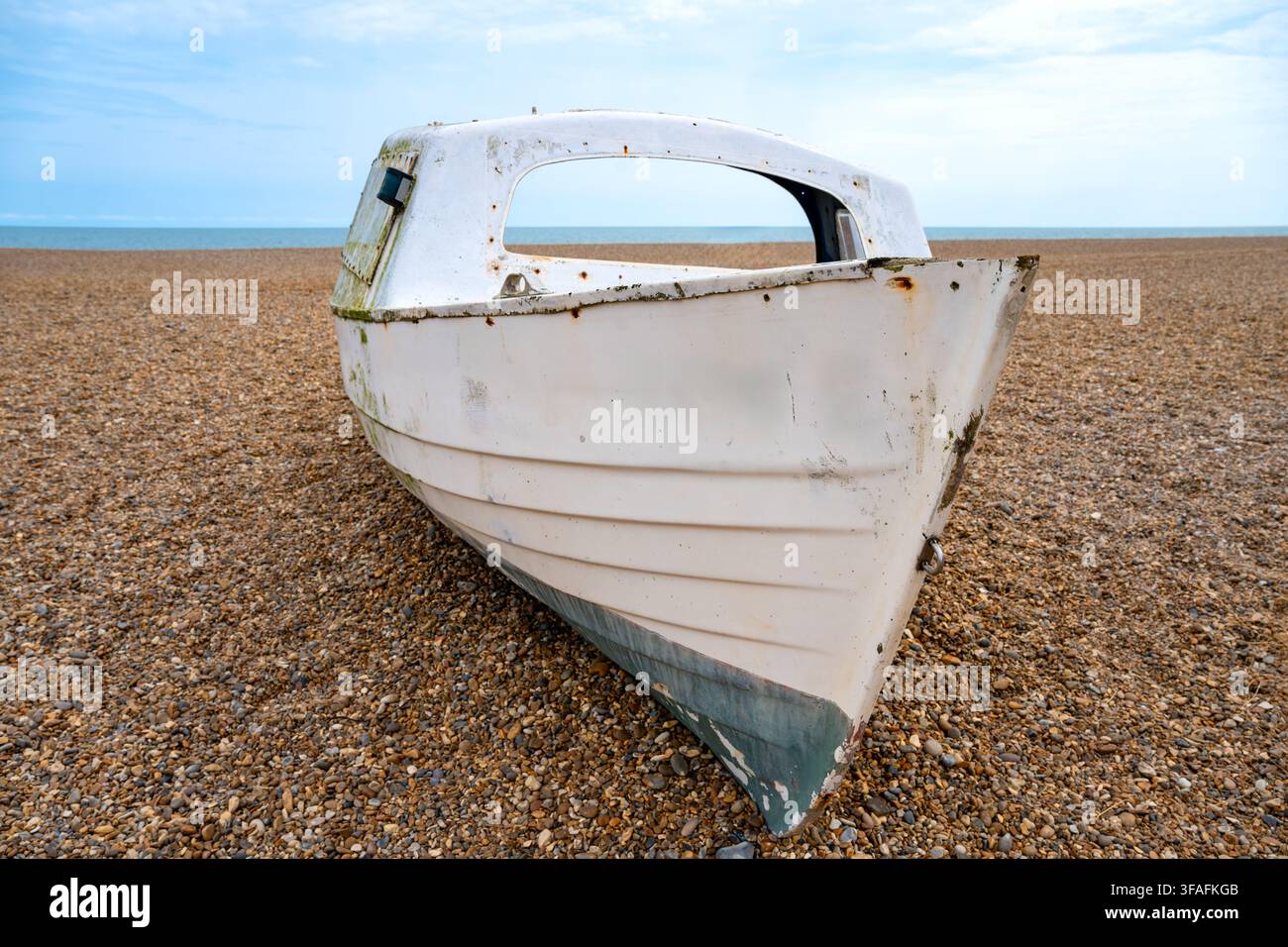 Ein verwittertes altes Fischerboot ruht auf dem Kieselstrand in Aldeburgh, Suffolk, sein weißer Rumpf abgenutzt und verrostet. Die ruhige Nordsee erstreckt sich bis zum Stockfoto