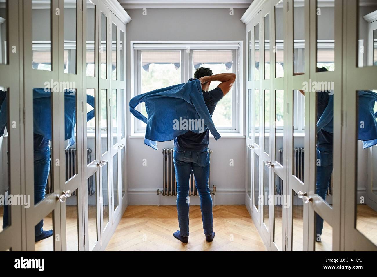 Mann, Fenster und Ankleide mit Hemd im Flur oder Schrank für Mode oder Vorbereitung zu Hause. Rückansicht, männliche Person oder sich im Korridor fertig machen mit Stockfoto