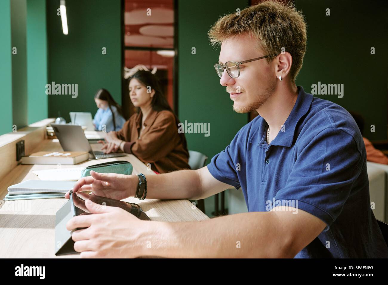 Verschiedene Studierende studieren mit digitalen Geräten in der Campus-Bibliothek Stockfoto