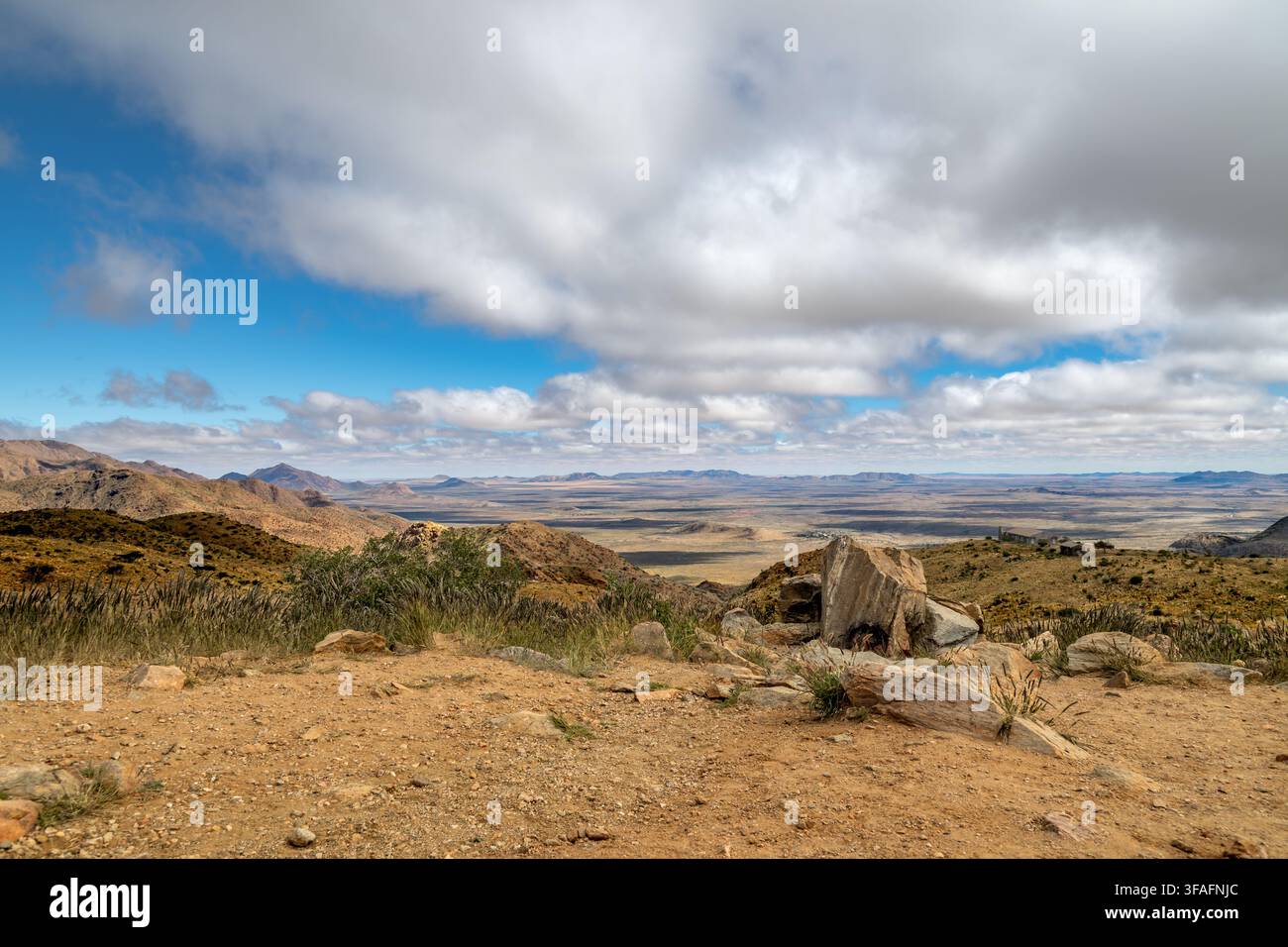 Panoramarundblick vom Spreetshoogte-Pass in Namibia. Eine weite, trockene Landschaft erstreckt sich unter einem strahlend blauen Himmel, der mit flauschigen weißen Wolken übersät ist. T Stockfoto