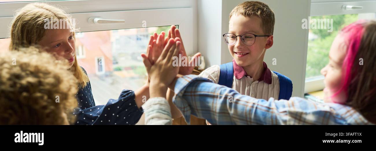 Fröhliche verschiedene Kinder geben ein High Five im Schulklassenzimmer Stockfoto
