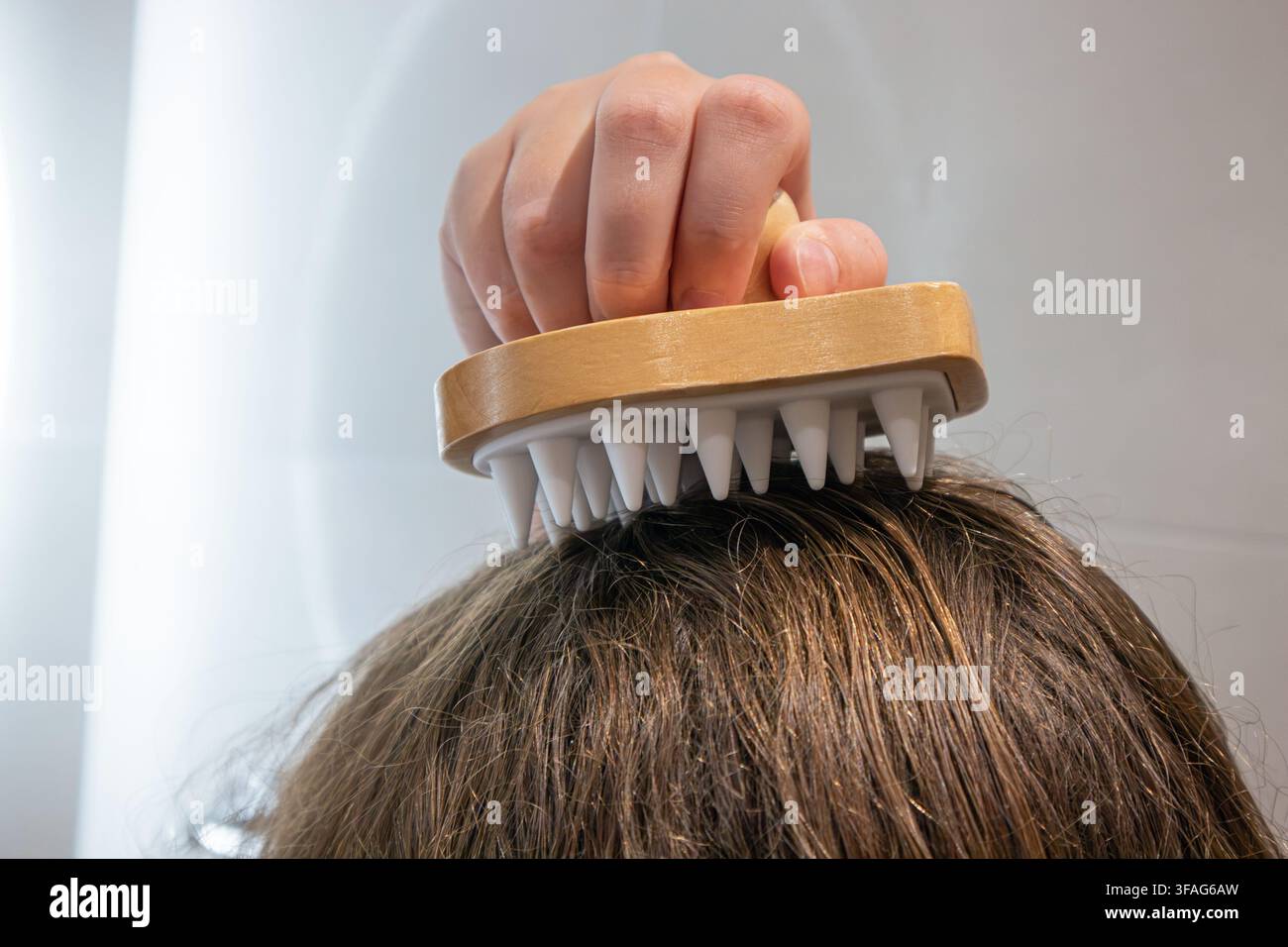 Ein Mädchen verwendet einen Kopfmassagegerät aus Holz und Silikon, um ihren Kopf in einem Badezimmer zu Hause zu massieren. Stockfoto