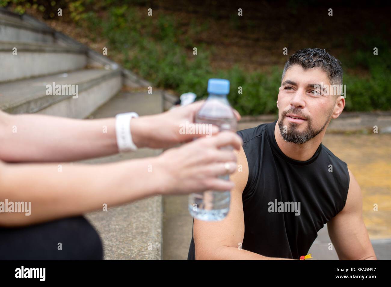 Sportliche Frau sitzt auf Außentreppen und trinkt Wasser aus der Flasche, während sie sich nach dem Training ausruht und hydriert. Stockfoto