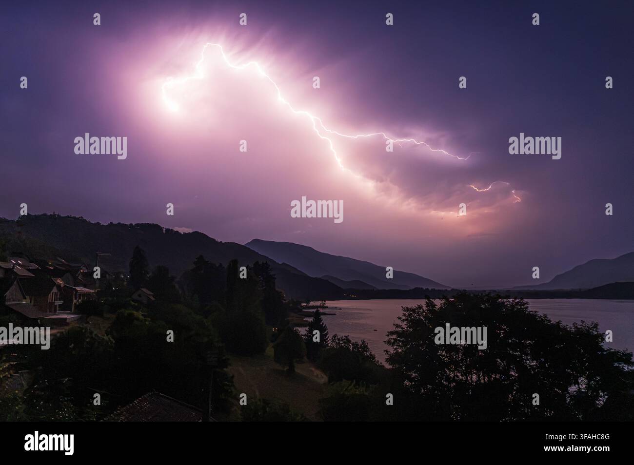 Massenblitz eines Gewitters am Himmel, der ein kleines Dorf an einem See in der Nacht im Südosten Frankreichs beleuchtet Stockfoto