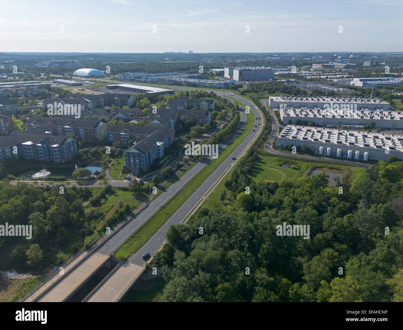 ASHBURN, VIRGINIA, USA - 8. AUGUST 2026: Drohnen-Luftaufnahme von Wohngebäuden, einer geteilten Straße und einem Amazon Web Services-Rechenzentrumskampus. Stockfoto