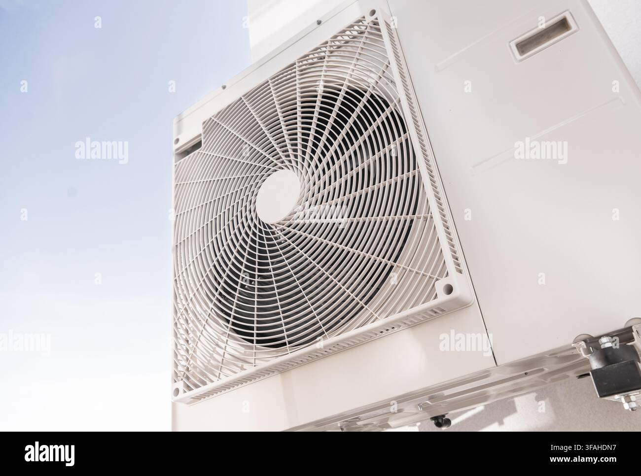 Eine Klimaanlage ist an einer weißen Wand installiert. Die Sonne scheint hell im Hintergrund. Diese Szene zeigt die Bedeutung von Kühlsystemen i Stockfoto