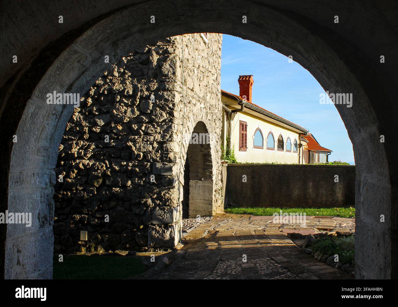Steinerne Bogendurchfahrt umrahmt mittelalterliche Stadtmauern und historisches Gebäude unter klarem blauem Himmel in der Altstadt Kastav, Region Kvarner, Kroatien. Stockfoto
