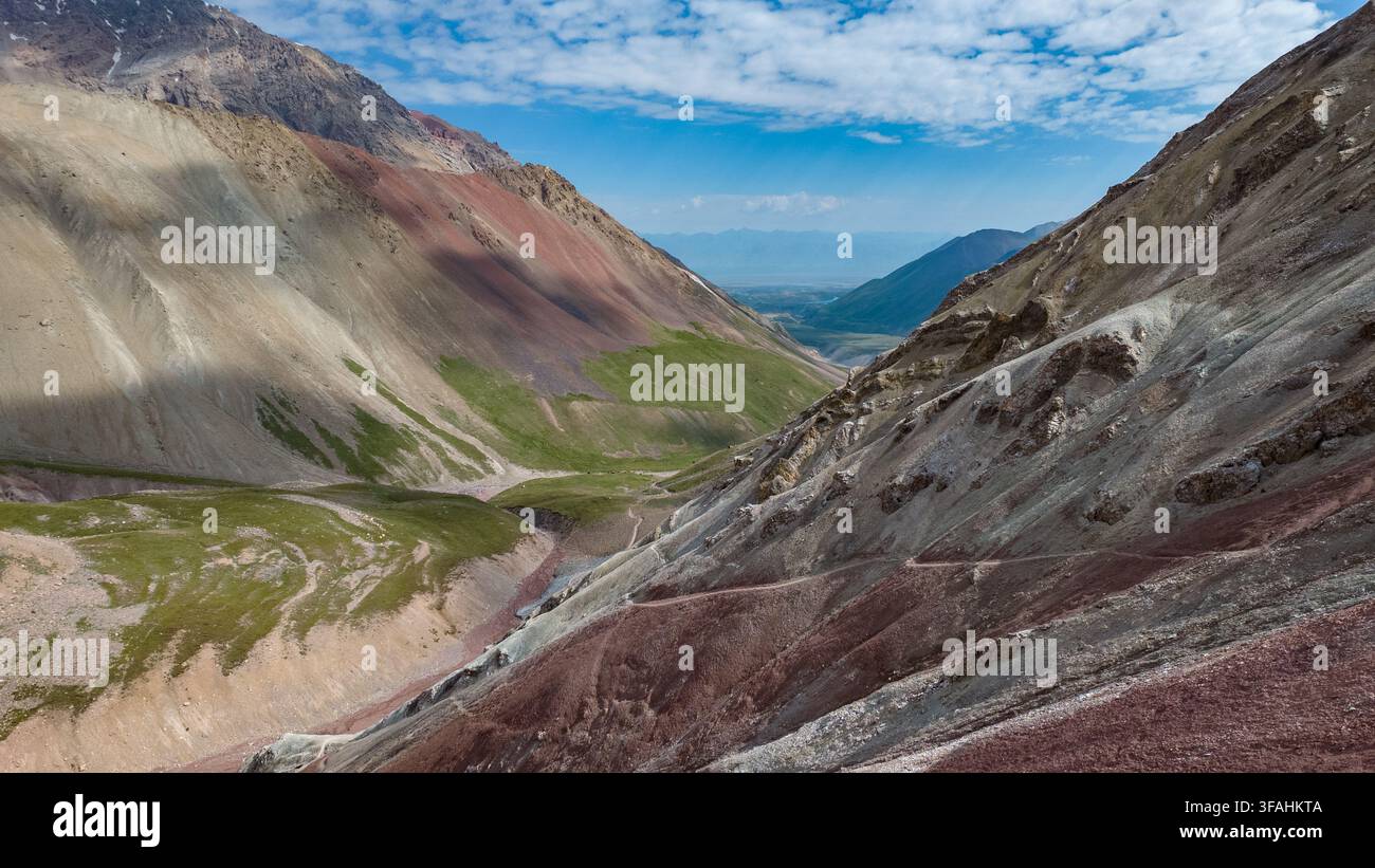Die Ansicht zeigt farbenfrohe Hügel und Täler in Kirgisistan. Die Szene fängt die natürlichen Merkmale der Gegend mit Grünflächen und felsigen Oberflächen unter einem Stockfoto