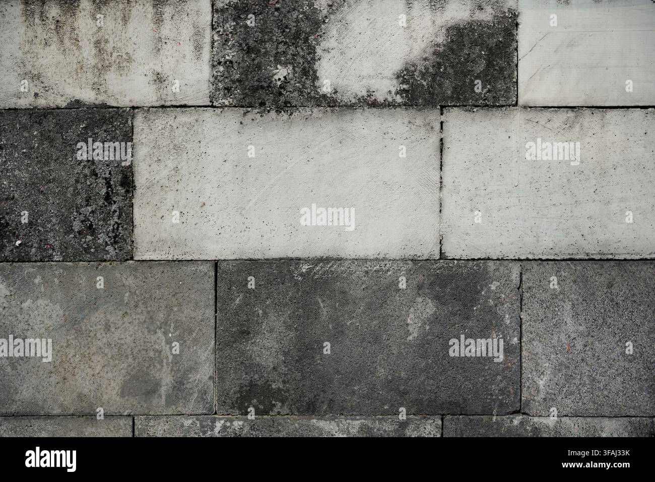 Ein strukturierter Hintergrund mit einer verwitterten Wand aus gemischten hellen und dunklen grauen Betonblöcken. Zeigt Anzeichen von Alterung, Grunge und Rauheit. Stockfoto