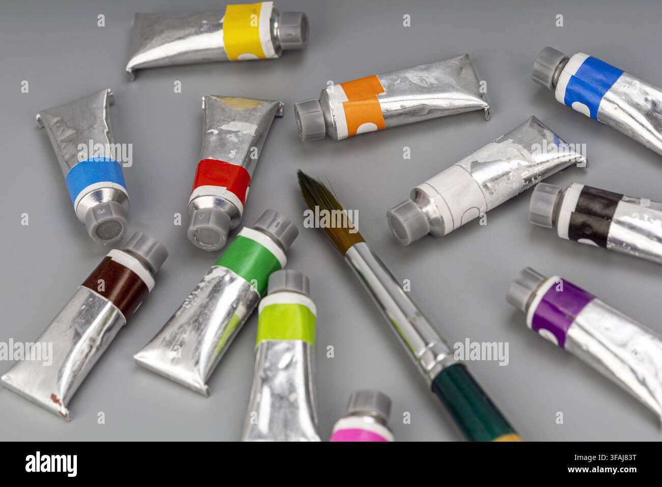 Bunte Wasserfarbtuben in Metallhüllen mit einem spitzen Kunstpinsel, der auf einem modernen grauen Hintergrund für kreatives Malen und künstlerische Hobbearbeit liegt. Stockfoto