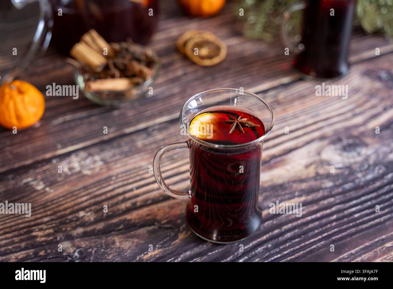 Warmes Glas hausgemachten Glühweins, garniert mit Sternanis, serviert auf einem rustikalen Holztisch, umgeben von Zimtstangen, getrockneten Orangenscheiben und Fes Stockfoto