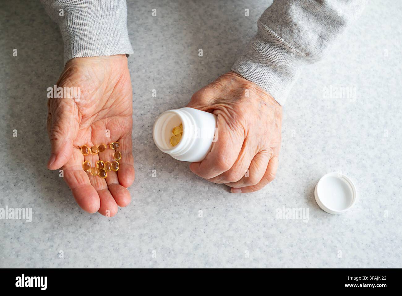 Ältere Hände schütten Vitaminkapseln aus einer Medikamentenflasche für die tägliche Gesundheits- und Pflegeroutine Stockfoto