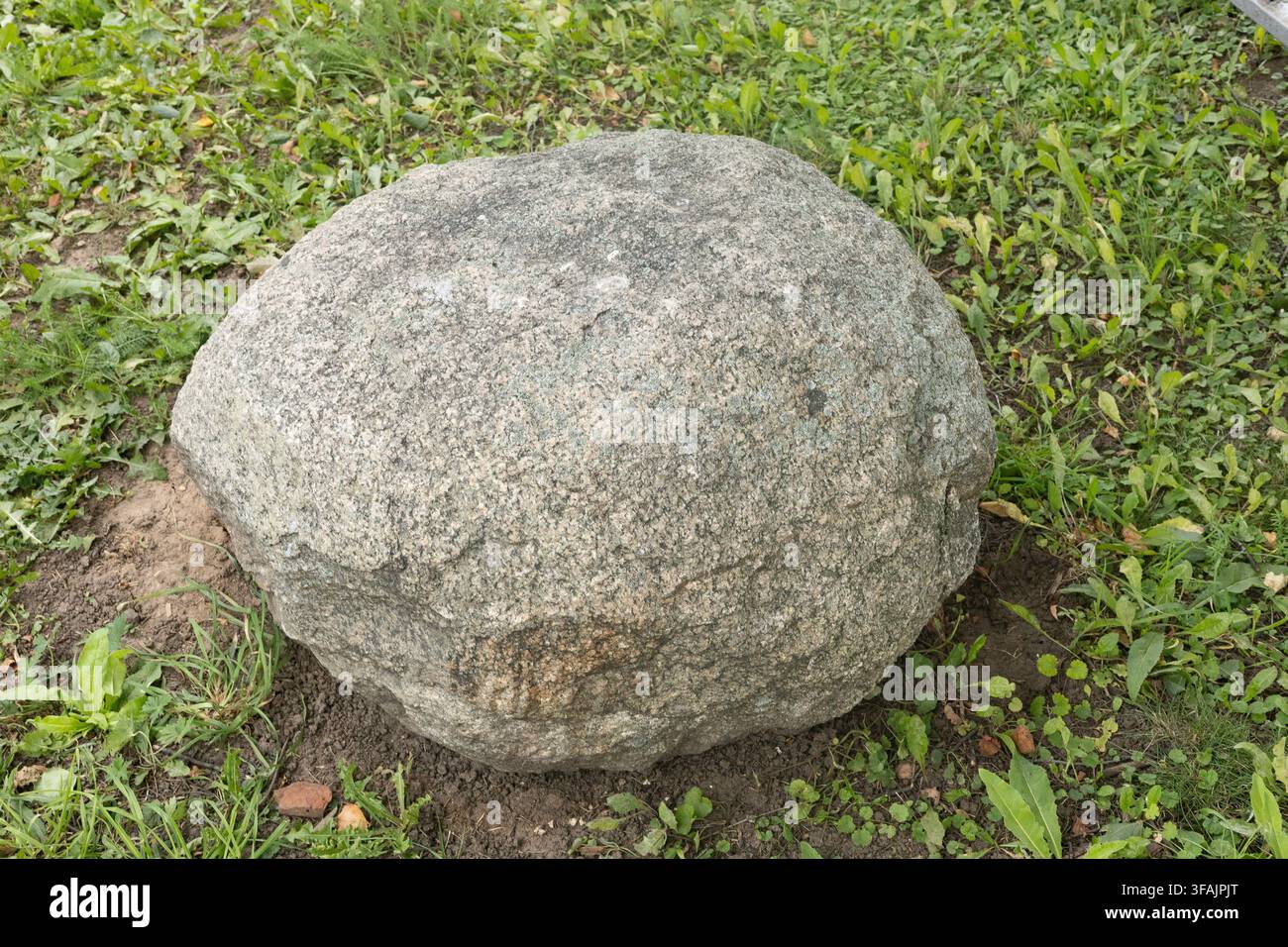Großer runder Granitblock auf einem grünen Grasfeld. Stockfoto