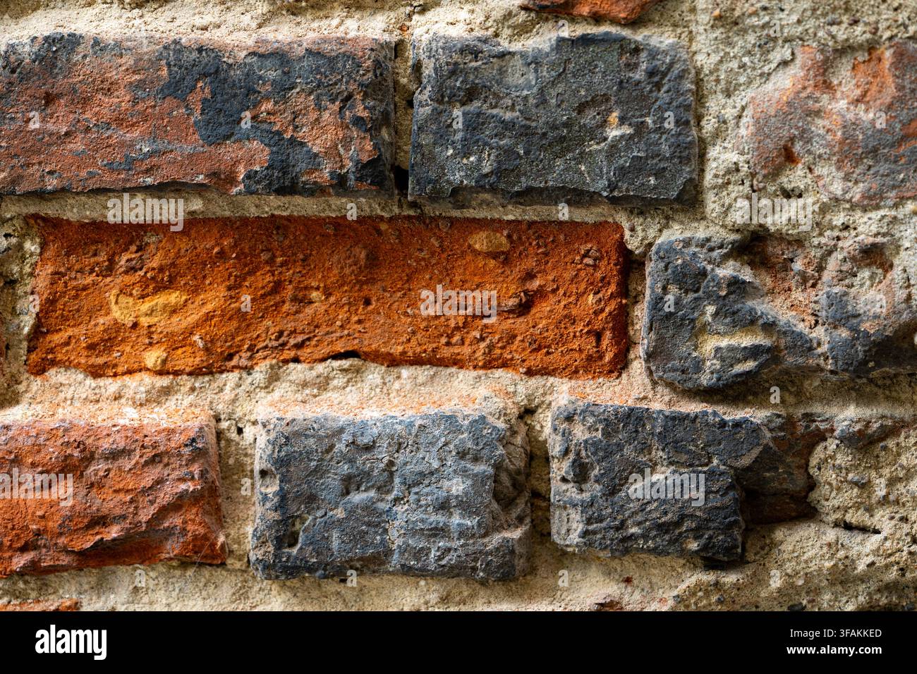 Eine verwitterte Ziegelmauer zeigt unregelmäßige Mauerarbeit mit gemischten grauen und braunen Tönen. Raue Oberflächen und unterschiedliche Mörtellinien. Stockfoto