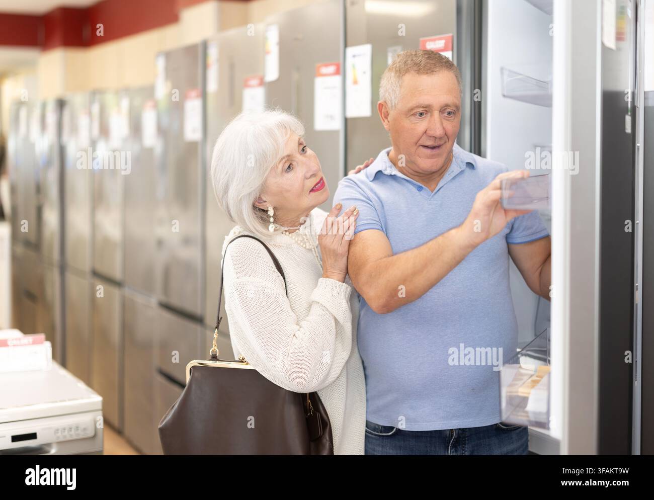 Älteres Ehepaar steht in einem Baumarkt und wählt einen Kühlschrank Stockfoto