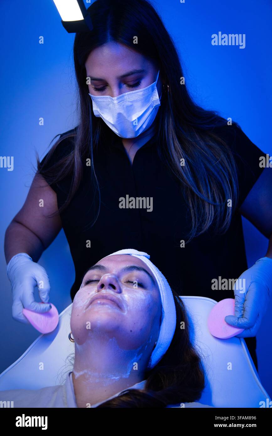 Krankenschwester wischt Hautpflegeprodukt von den Wangen des Patienten Stockfoto