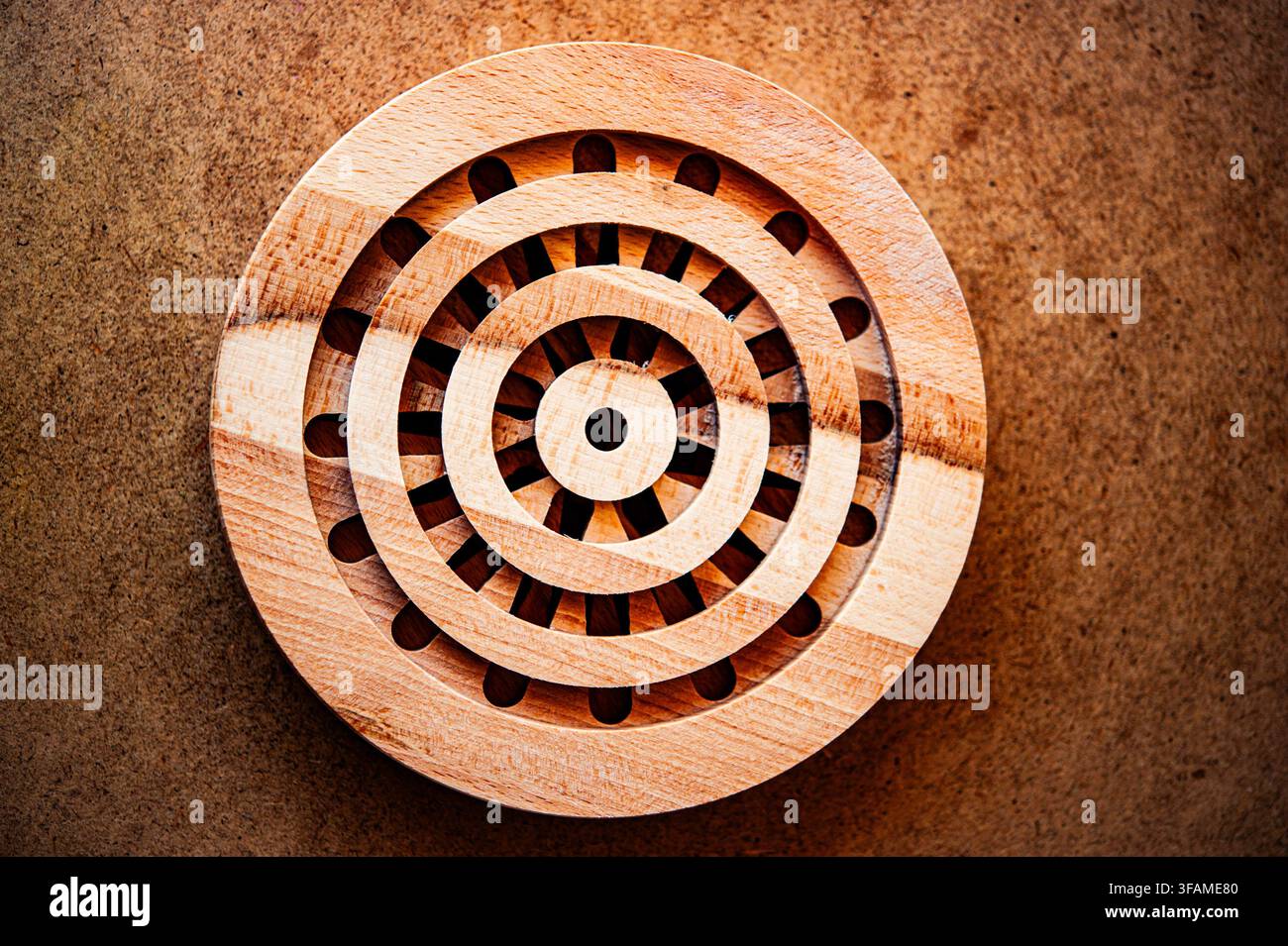 Oberansicht eines kreisförmigen, geschichteten Holzpuzzles mit radialen Schlitzen auf einer braunen, texturierten Oberfläche, das geometrisches Handwerk und natürliche Holzmaserung betont Stockfoto