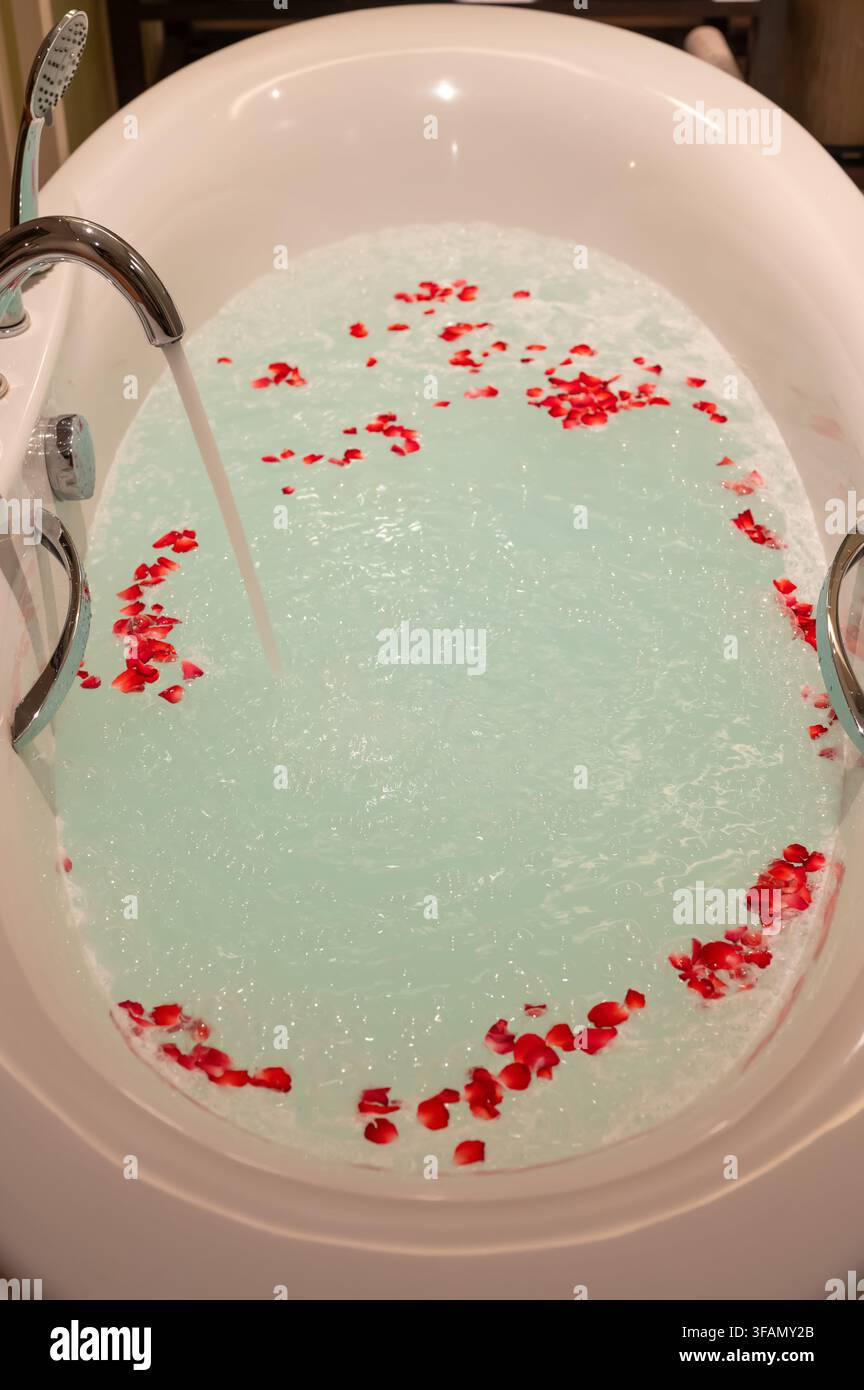 Badewanne, die sich mit Wasser und roten Rosenblättern füllt. Stockfoto