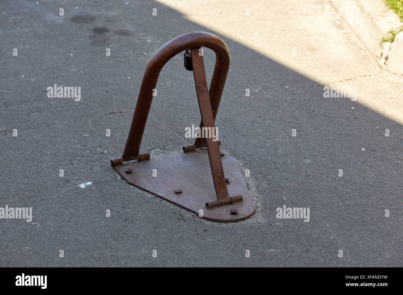 Ein braunes Metallklapp-Parkbarrierenschloss ist auf der grauen Asphaltfläche installiert. Die manuelle Anti-Parkvorrichtung ist mit einem Vorhängeschloss gesichert, um Reserv Stockfoto