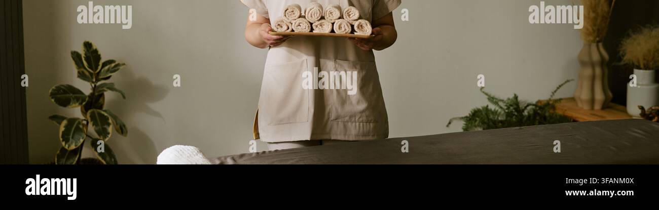 Kopf einer weiblichen Therapeutin, die ein Tablett mit gerollten Handtüchern in einem Spasalon hält Stockfoto