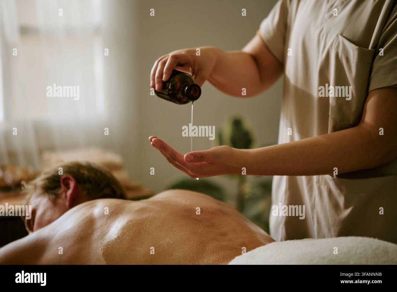 Masseur gießt ätherisches Öl auf die Hand für eine Rückenmassage des Mannes Stockfoto