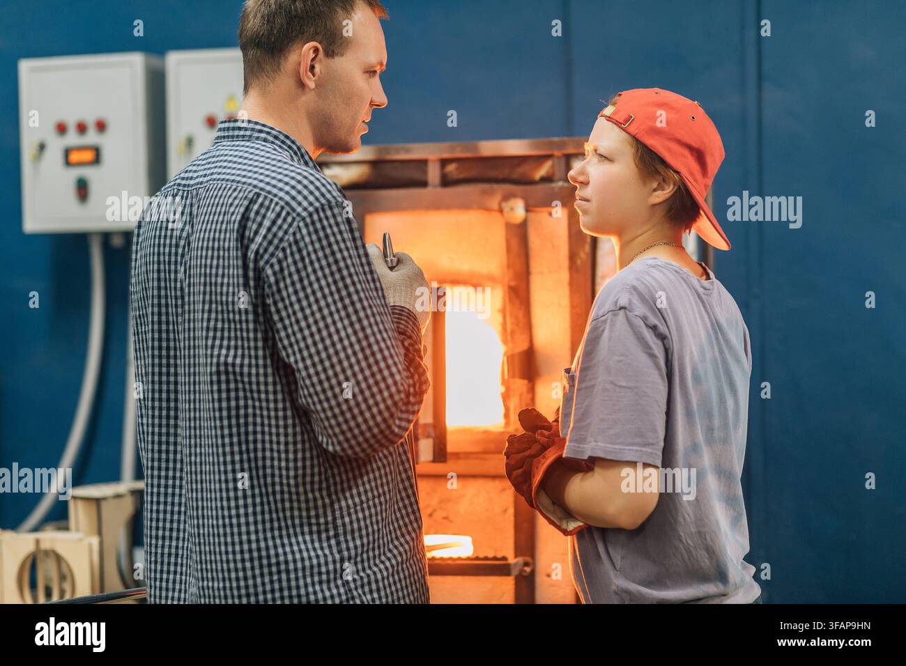 Mann lehrt Schüler Glasblasen am heißen Ofen Stockfoto