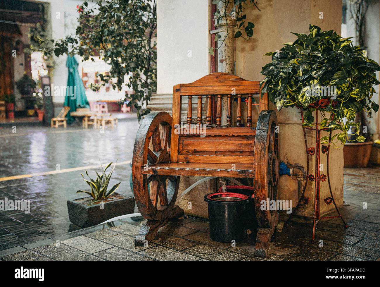 Rustische Holzbank mit Wagenrädern auf einer nassen Terrasse Stockfoto